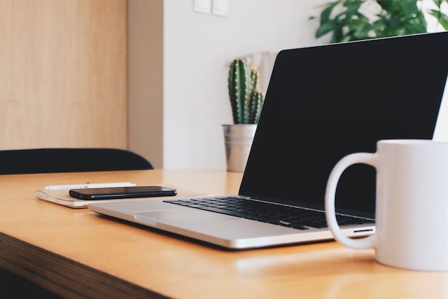 A laptop and phone sitting on top of a wooden table.